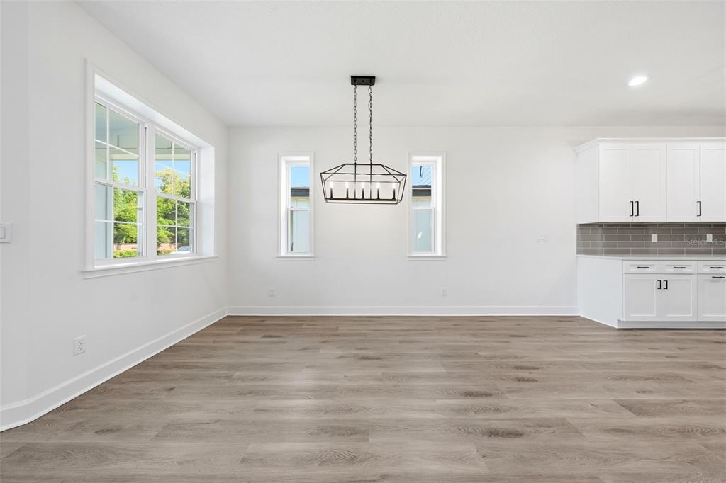 A dining area with wood-look flooring, white walls, a geometric chandelier, and adjacent white kitchen — 1018 FARMSTEAD STREET, EUSTIS, FL
