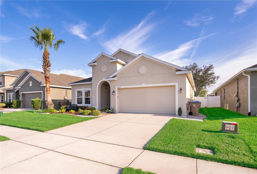 A beige, single-story suburban house with a two-car garage and a palm tree in front — 2587 TANNER TERRACE, KISSIMMEE, FL