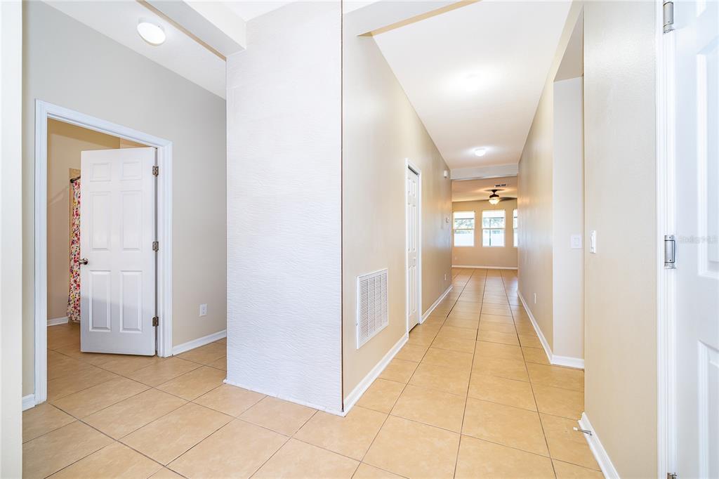 A hallway with tan tile flooring leads toward a room with windows and a ceiling fan — 2587 TANNER TERRACE, KISSIMMEE, FL