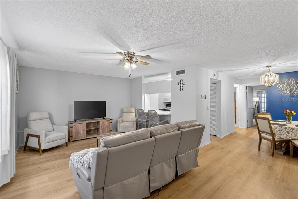 A living room with light wood flooring, a grey sofa, and an open kitchen area — 11920 DIETZ DRIVE UNIT 11920, TAMPA, FL