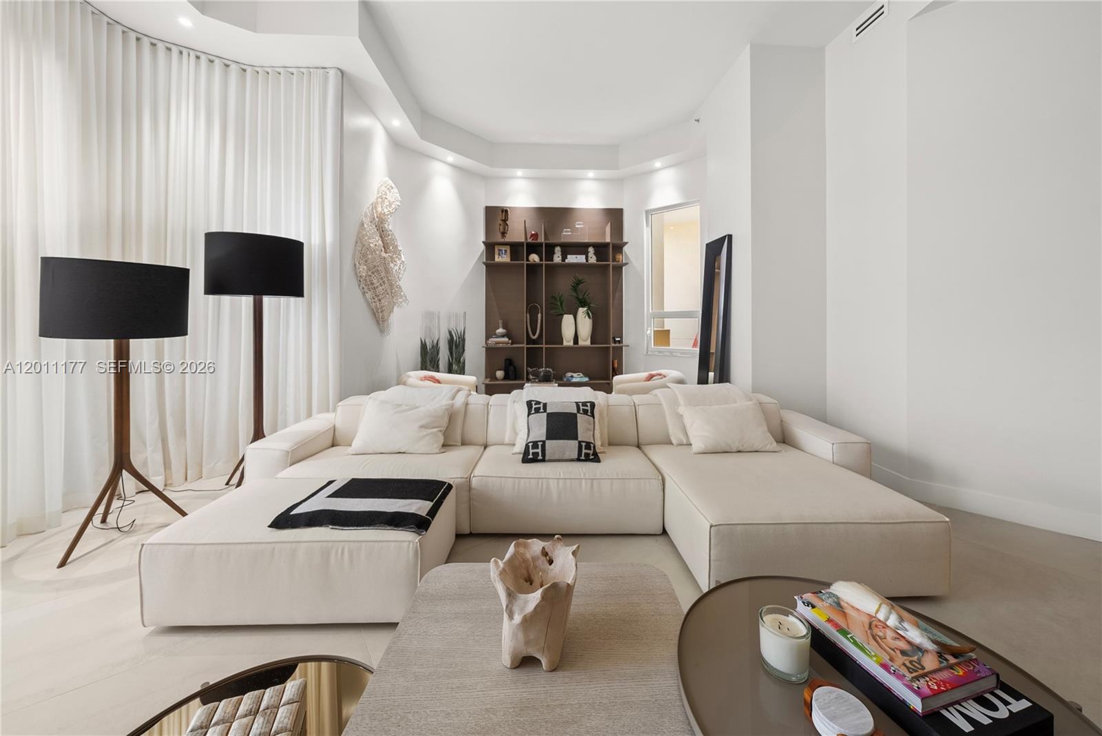A modern living room features a large white sectional sofa, a bookshelf, and floor lamps — 808 Brickell Key Dr # 408, Miami FL 33131, MIAMI, FL