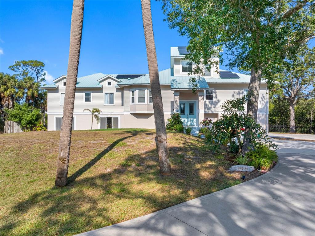 A two-story house with light siding, a metal roof, and solar panels sits on a lot — 1580 MACCHESNEY DRIVE, TARPON SPRINGS, FL