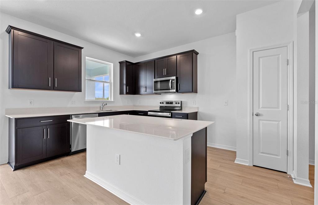 A kitchen features dark wood cabinets, white countertops, a central island, and light wood flooring — 1277 LAKERIDGE WAY, LAKE ALFRED, FL