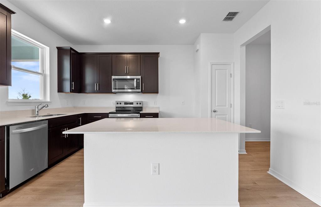 A kitchen features dark wood cabinets, stainless steel appliances, a white island, and light flooring — 1277 LAKERIDGE WAY, LAKE ALFRED, FL