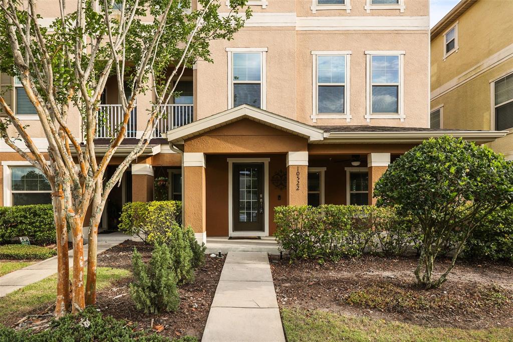 A three-story townhouse exterior with a covered front porch, tan stucco, and a concrete walkway — 10522 GREEN IVY LANE, ORLANDO, FL