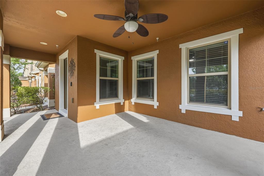 A covered patio with a ceiling fan, three windows, and light-colored concrete flooring — 10522 GREEN IVY LANE, ORLANDO, FL