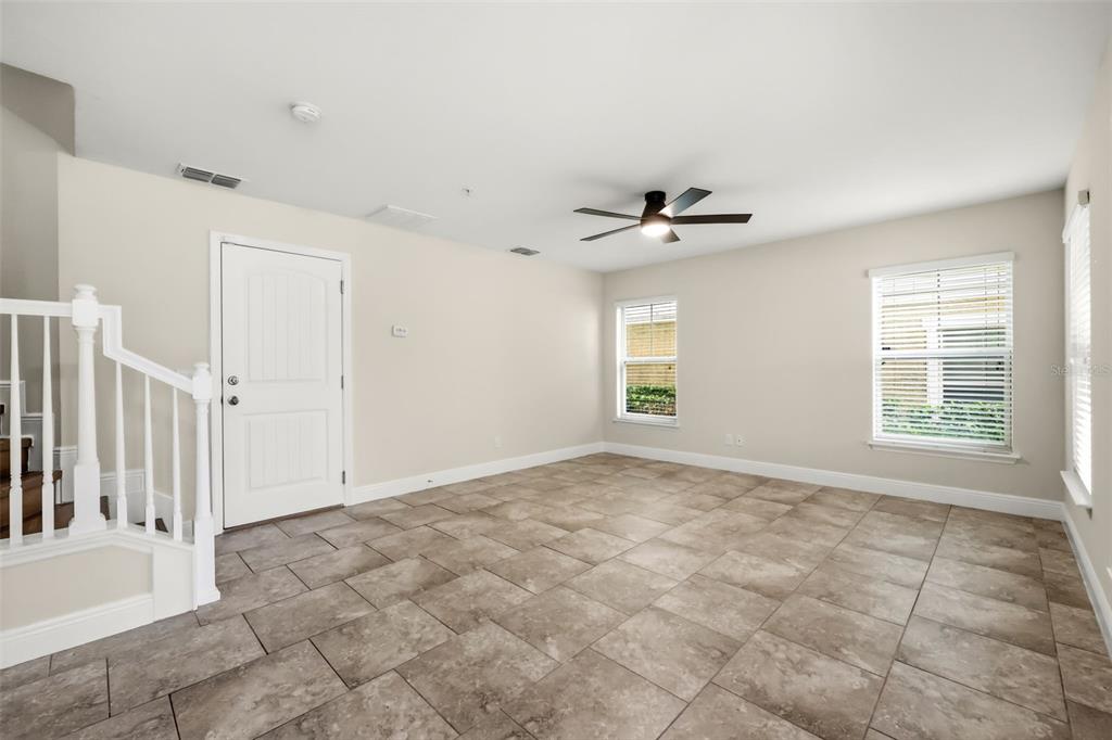 An empty room features light-colored walls, large tile flooring, a ceiling fan, and a staircase — 10522 GREEN IVY LANE, ORLANDO, FL