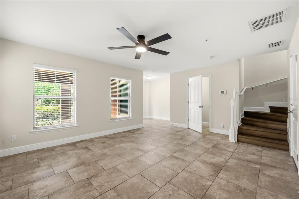 A room with beige walls, tile flooring, a ceiling fan, and stairs on the right — 10522 GREEN IVY LANE, ORLANDO, FL