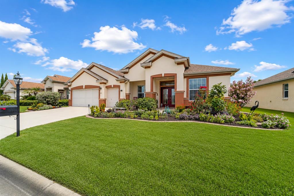 A single-story house with a beige stucco exterior, a three-car garage, and a landscaped yard — 9361 SE 137TH STREET ROAD, SUMMERFIELD, FL
