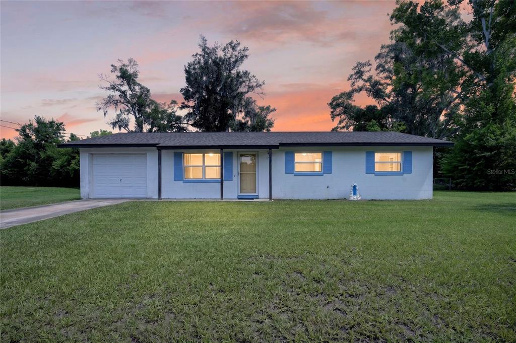 A single-story white house with a garage and blue shutters sits on a grassy lawn — 1901 NE 52ND STREET, OCALA, FL