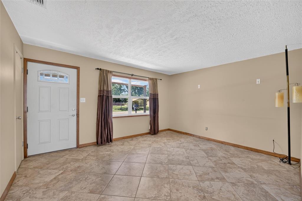 An empty room with beige walls, tile flooring, a front door, and a window — 1901 NE 52ND STREET, OCALA, FL