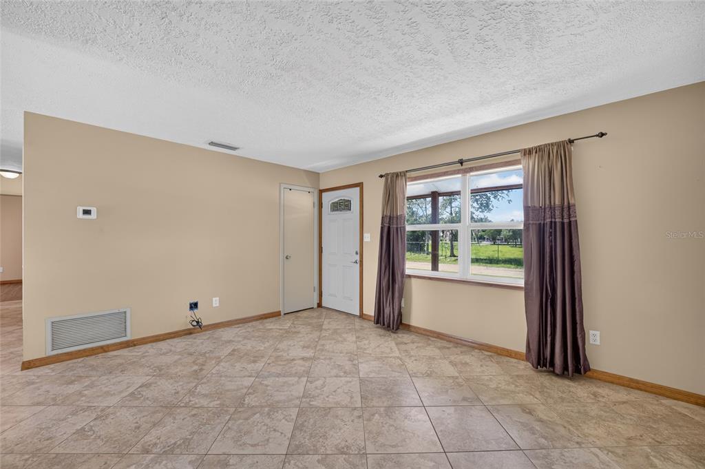 A living room features beige walls, tile flooring, a white front door, and a window — 1901 NE 52ND STREET, OCALA, FL