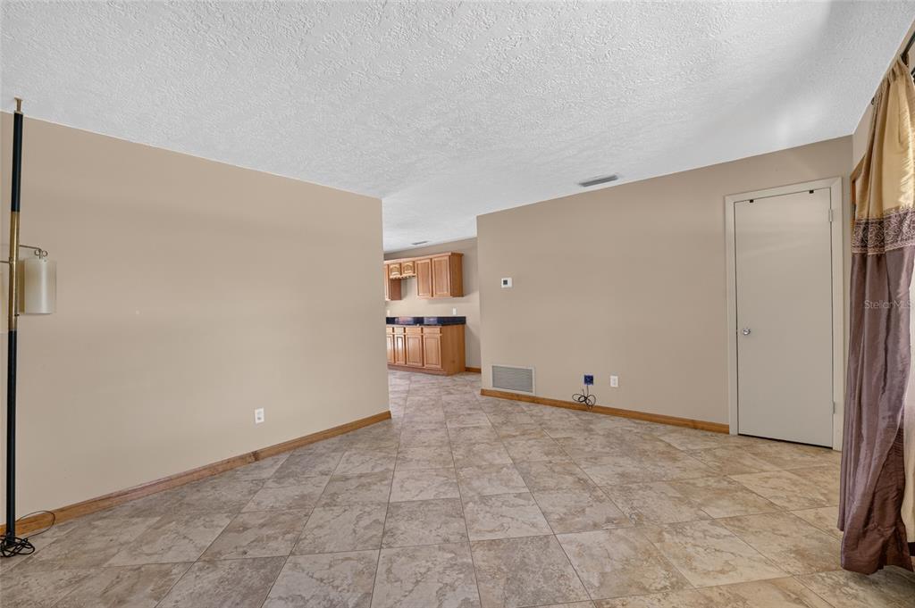 A room with beige walls and tiled flooring leads into a kitchen with wooden cabinets — 1901 NE 52ND STREET, OCALA, FL
