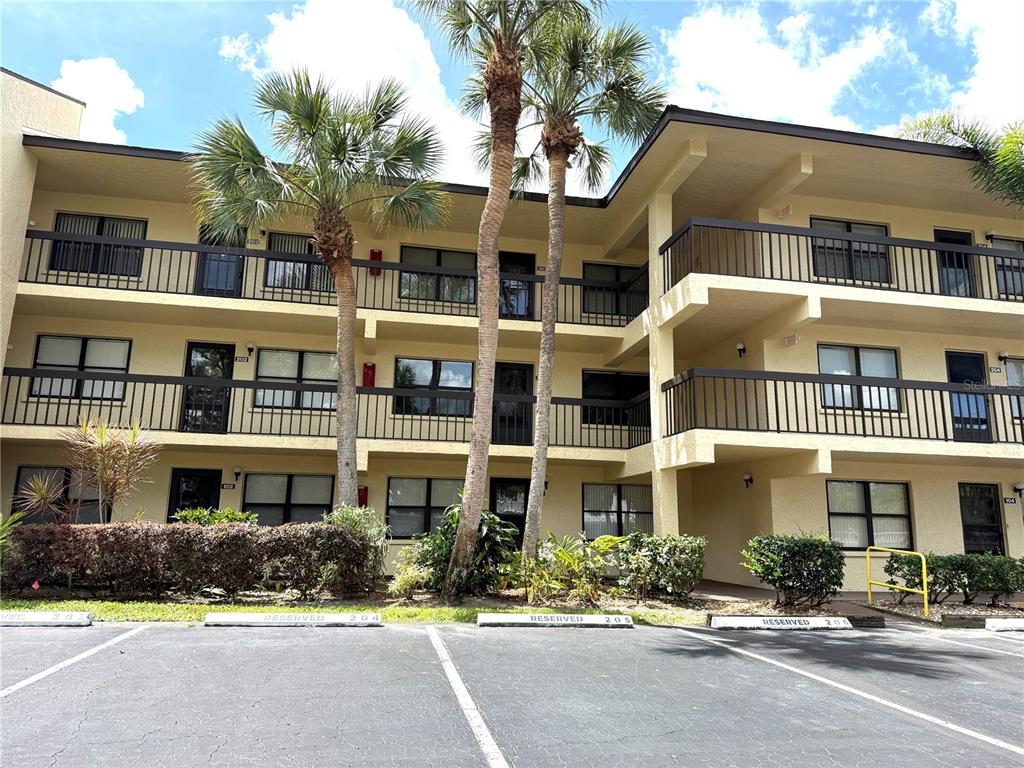 A three-story apartment building with tan stucco walls, dark railings, and palm trees in front — 425 30TH AVENUE W UNIT C204, BRADENTON, FL