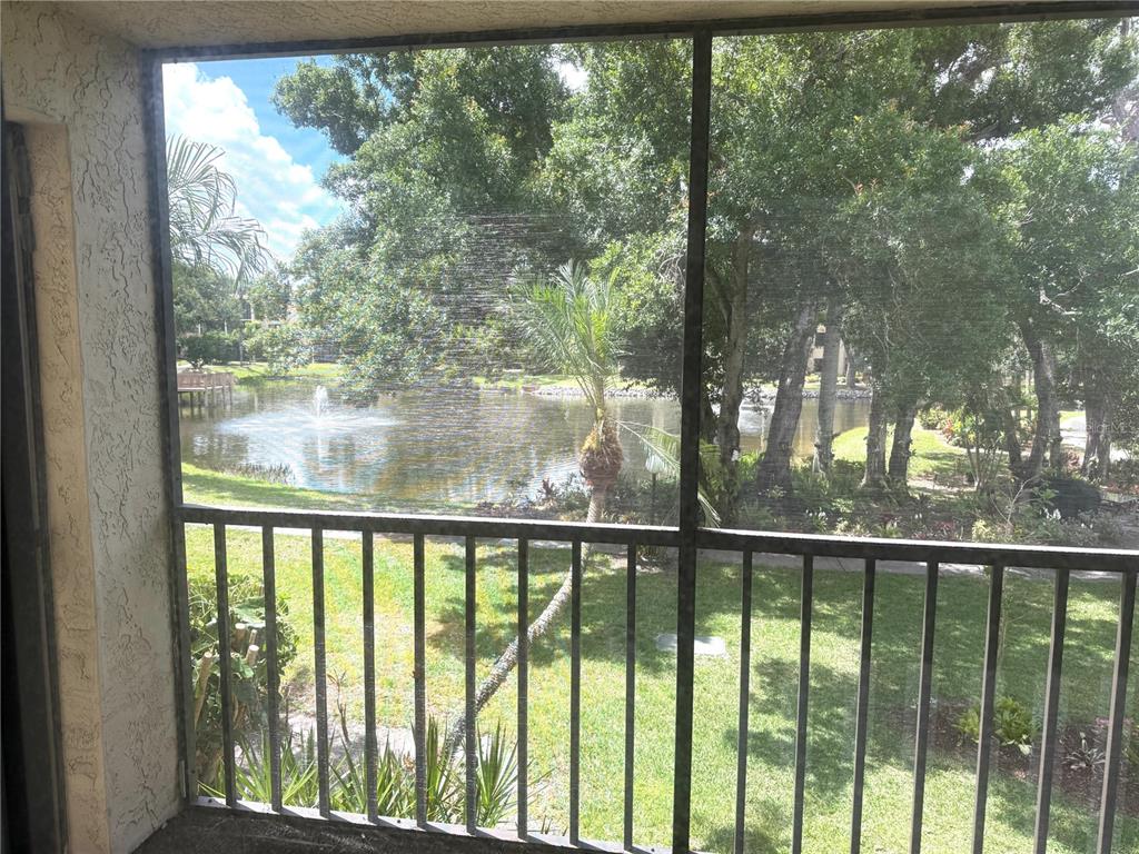 A screened-in balcony overlooks a grassy lawn, trees, and a pond with a fountain — 425 30TH AVENUE W UNIT C204, BRADENTON, FL