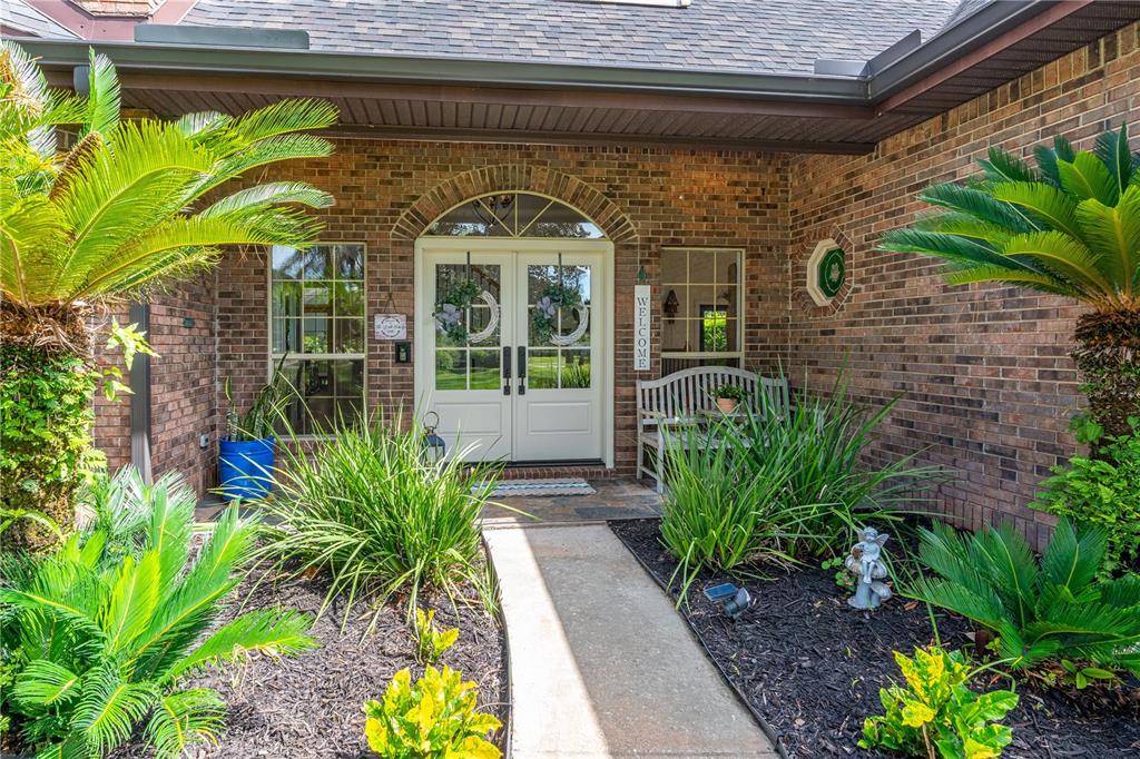 The front entrance of a brick house features double doors, a walkway, and potted plants — 73 SHADOW CREEK WAY, ORMOND BEACH, FL