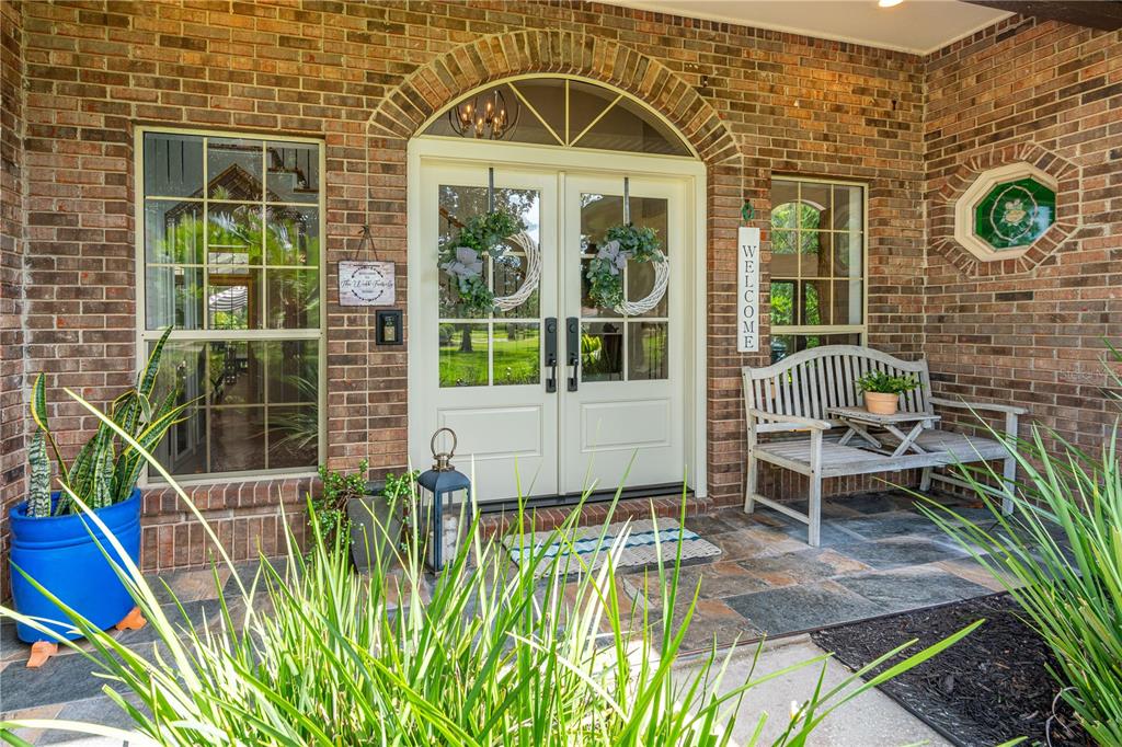 A brick-front entryway features double doors, a wooden bench, and potted plants on a patio — 73 SHADOW CREEK WAY, ORMOND BEACH, FL