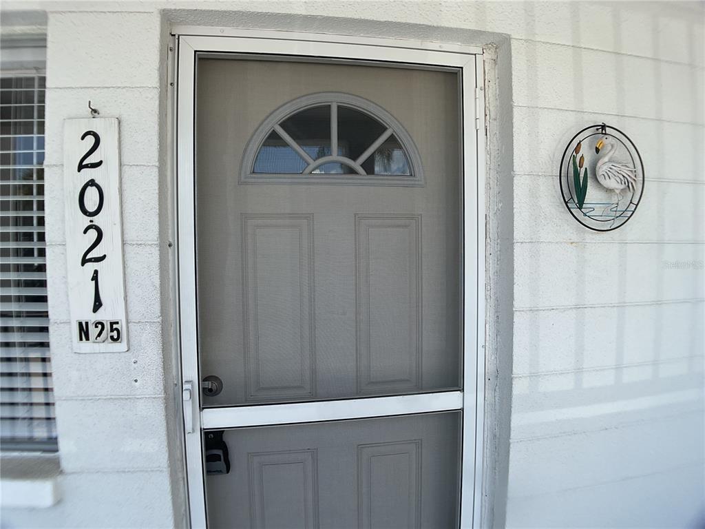 A gray storm door with a decorative arched window sits beside a vertical house number sign — 2021 CANAL DRIVE UNIT N25, BRADENTON, FL