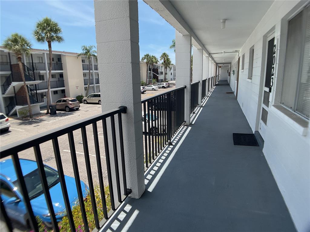 An outdoor apartment walkway features a black metal railing overlooking a parking lot with palm trees — 2021 CANAL DRIVE UNIT N25, BRADENTON, FL