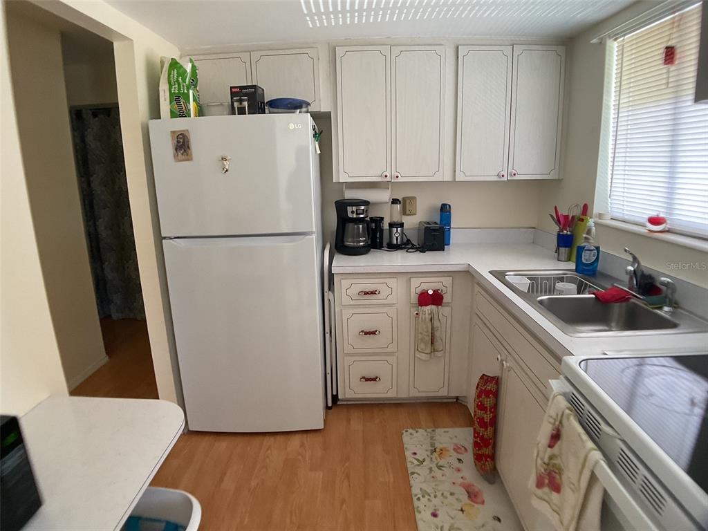 A kitchen features white cabinets, a white refrigerator, a double sink, and light wood flooring — 2021 CANAL DRIVE UNIT N25, BRADENTON, FL