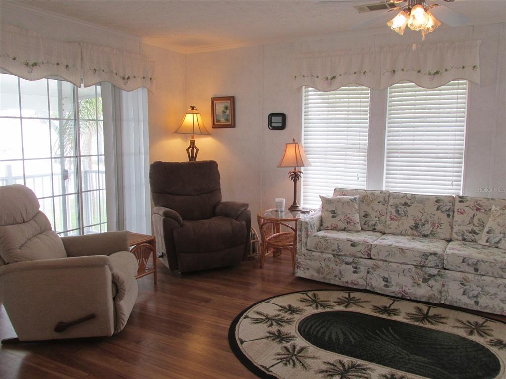 A living room features wood-look flooring, a floral sofa, two recliners, and a palm-patterned rug — 5 QUEEN OF WATERS STREET, LAKE WALES, FL