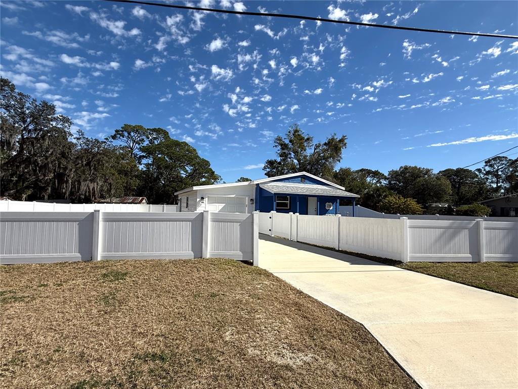 A blue house with a white fence and a concrete driveway under a blue sky — 2701 BROOKLINE AVENUE, NEW SMYRNA BEACH, FL