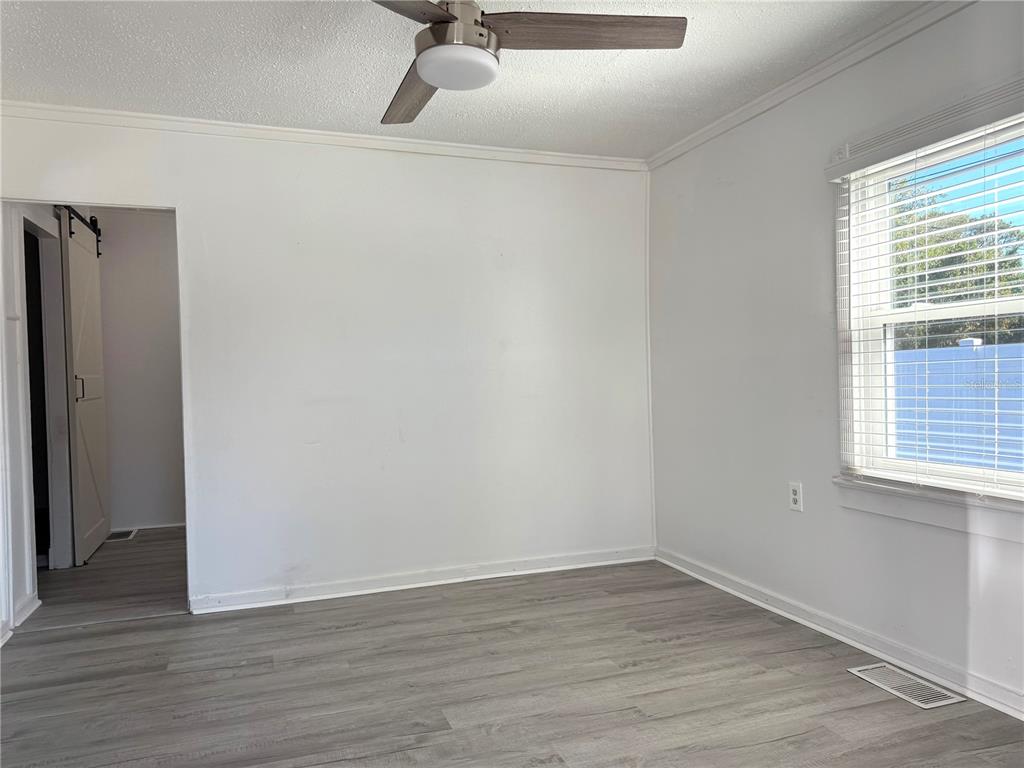 An empty room features white walls, gray wood-look flooring, a ceiling fan, and a window — 2701 BROOKLINE AVENUE, NEW SMYRNA BEACH, FL