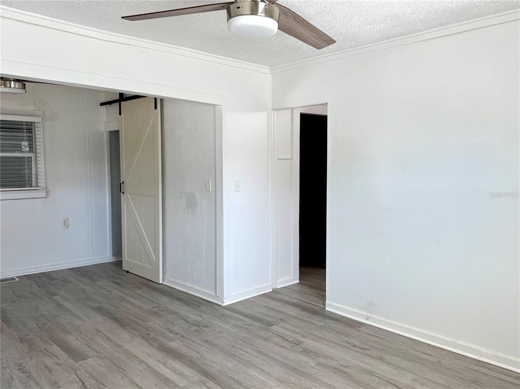 An interior room features white walls, light wood-look flooring, a ceiling fan, and a barn door — 2701 BROOKLINE AVENUE, NEW SMYRNA BEACH, FL