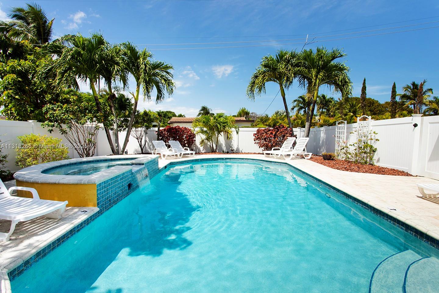 A swimming pool with an attached spa sits in a backyard with palm trees — 1311 Rodman St, Hollywood FL 33019, HOLLYWOOD, FL