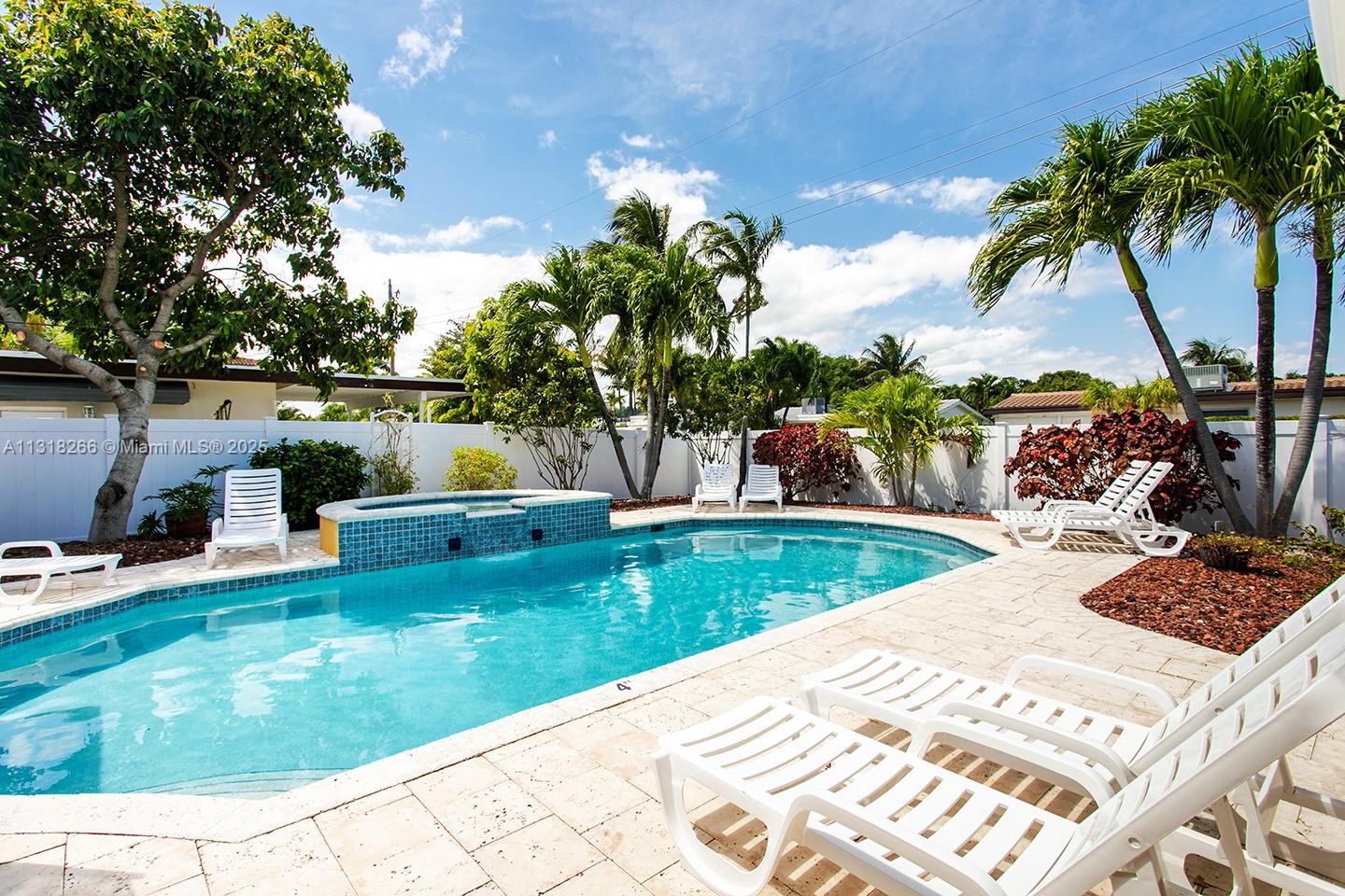 A backyard swimming pool with a spa, lounge chairs, and palm trees under a blue sky — 1311 Rodman St, Hollywood FL 33019, HOLLYWOOD, FL