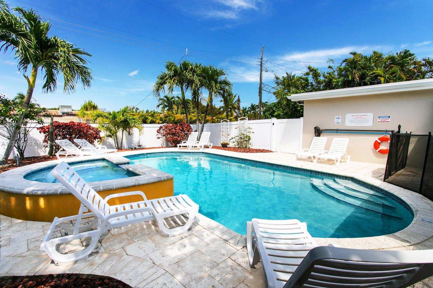 A backyard swimming pool and hot tub are surrounded by white lounge chairs and palm trees — 1311 Rodman St, Hollywood FL 33019, HOLLYWOOD, FL