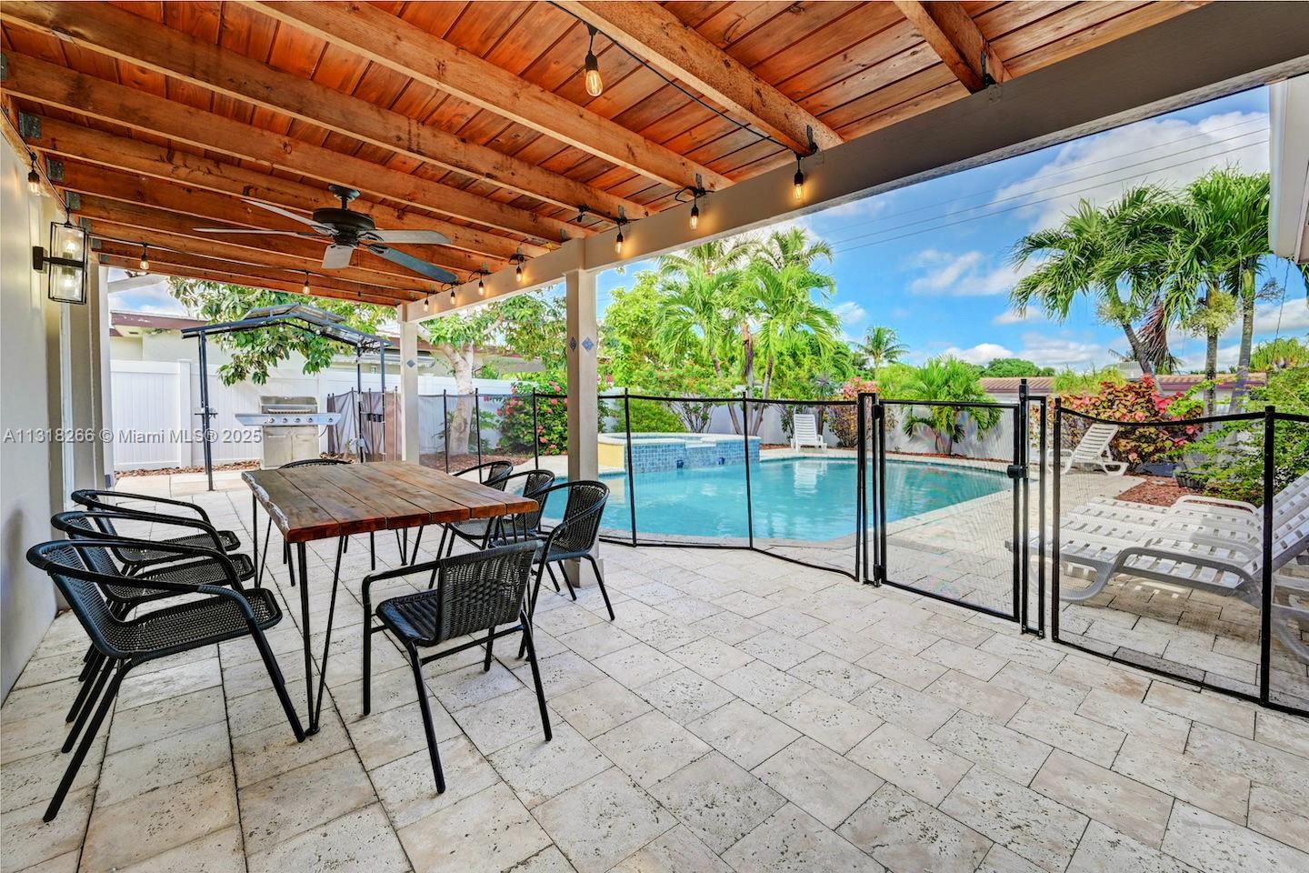 A covered patio with a dining set overlooks a fenced swimming pool and backyard — 1311 Rodman St, Hollywood FL 33019, HOLLYWOOD, FL