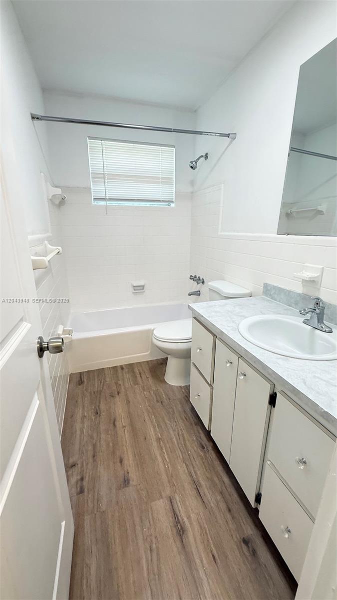 A bathroom features white tiled walls, a tub-shower combination, a vanity, and wood-look flooring — 400 SE 9th Ct # 9, Hallandale Beach FL 33009, HALLANDALE BEACH, FL
