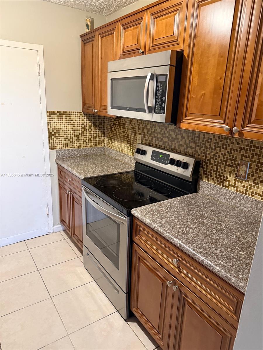 This kitchen features wood cabinets, stainless steel appliances, and a brown mosaic tile backsplash — 2000 NE 135th St # 403, North Miami FL 33181, NORTH MIAMI, FL