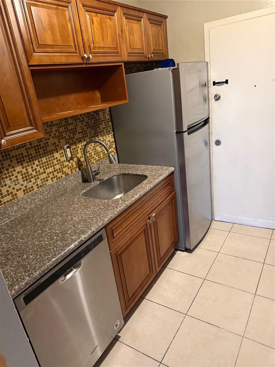 A kitchen features wood cabinets, granite countertops, a stainless steel dishwasher, and a refrigerator — 2000 NE 135th St # 403, North Miami FL 33181, NORTH MIAMI, FL