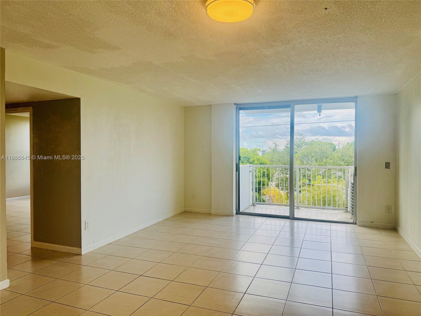 An empty room with beige tile flooring, white walls, and a sliding glass balcony door — 2000 NE 135th St # 403, North Miami FL 33181, NORTH MIAMI, FL