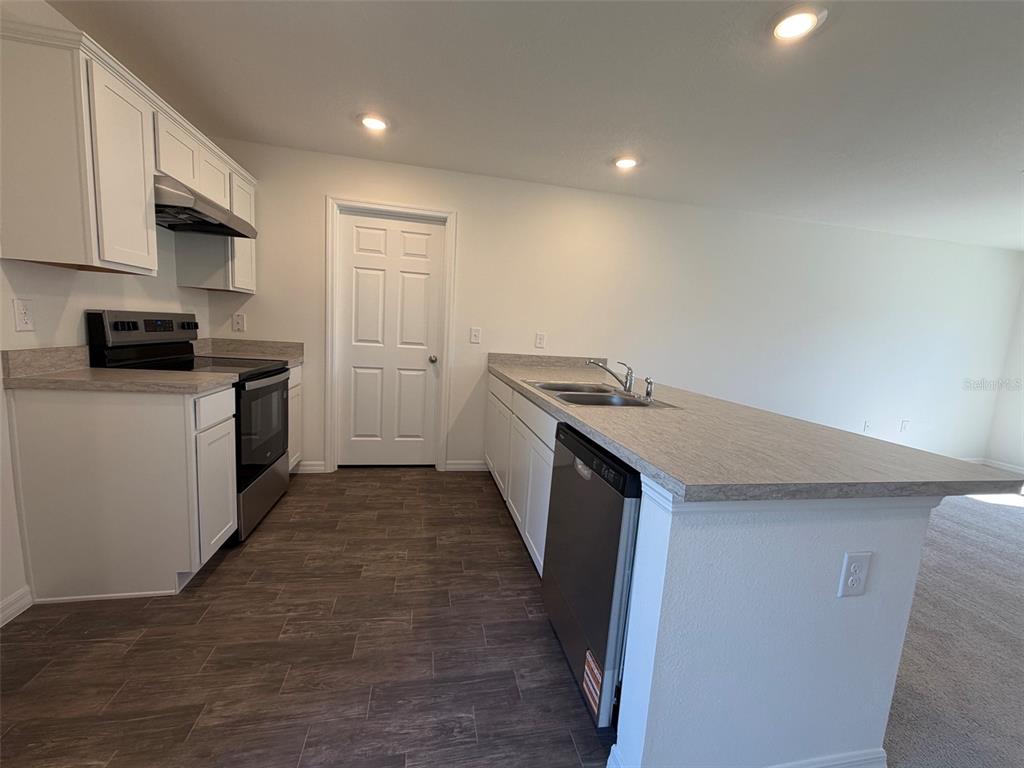 A kitchen features white cabinets, stainless steel appliances, a breakfast bar, and wood-look flooring — 219 SPOONBILL LANE, POINCIANA, FL