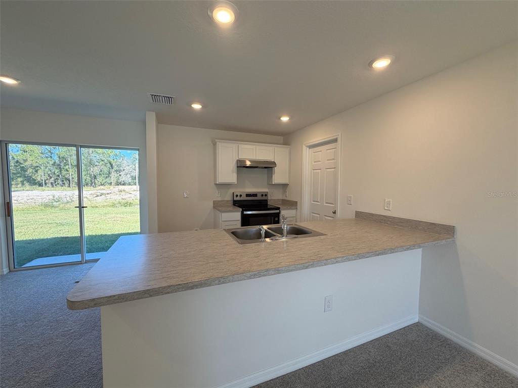 A kitchen features a breakfast bar, laminate countertops, white cabinets, and a sliding glass door — 219 SPOONBILL LANE, POINCIANA, FL