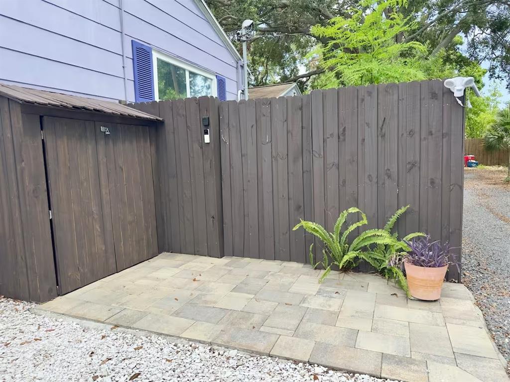 A paved patio area sits beside a wooden storage shed and a dark privacy fence — 5214 27TH AVENUE S UNIT 2, GULFPORT, FL