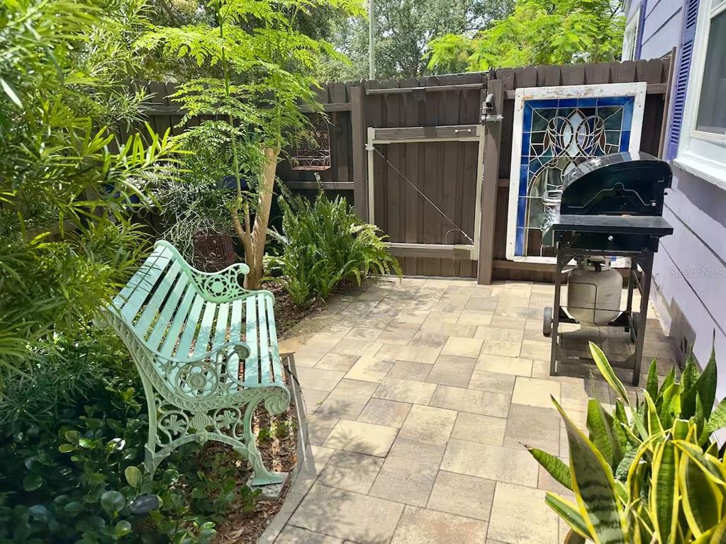A patio features a light green metal bench, a gas grill, and a stained glass window — 5214 27TH AVENUE S UNIT 2, GULFPORT, FL