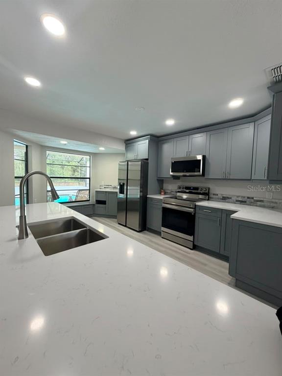 A modern kitchen features gray cabinets, white quartz countertops, stainless steel appliances, and a large island — 11189 LINDEN DRIVE, SPRING HILL, FL