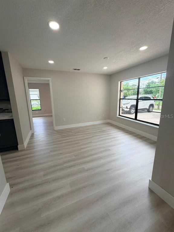 An empty room with light wood-look flooring, recessed lighting, and a large window — 11189 LINDEN DRIVE, SPRING HILL, FL