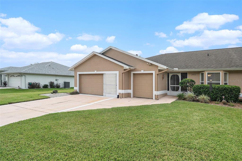 A tan single-story house features a two-car garage, a front entryway, and a green lawn — 29418 SCHINNECOCK HILLS LANE, SAN ANTONIO, FL
