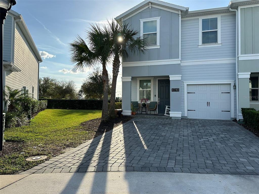 A two-story townhouse features a gray exterior, a paved driveway, and a small palm tree — 4740 TRIBUTE TRAIL, KISSIMMEE, FL