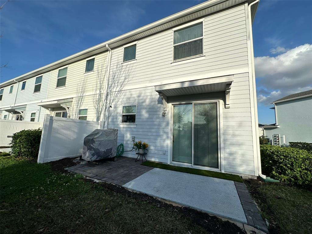 The exterior of a light-colored townhouse features a small concrete patio and sliding glass doors — 4740 TRIBUTE TRAIL, KISSIMMEE, FL
