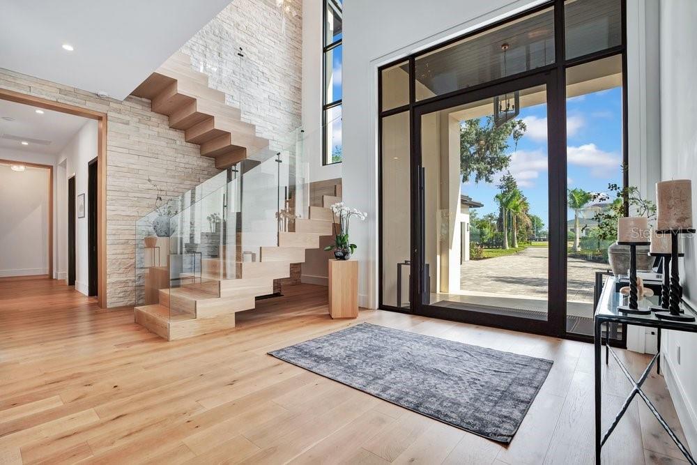 A modern entryway features light wood flooring, a floating staircase, and a large glass door — 724 W 2ND AVENUE, WINDERMERE, FL