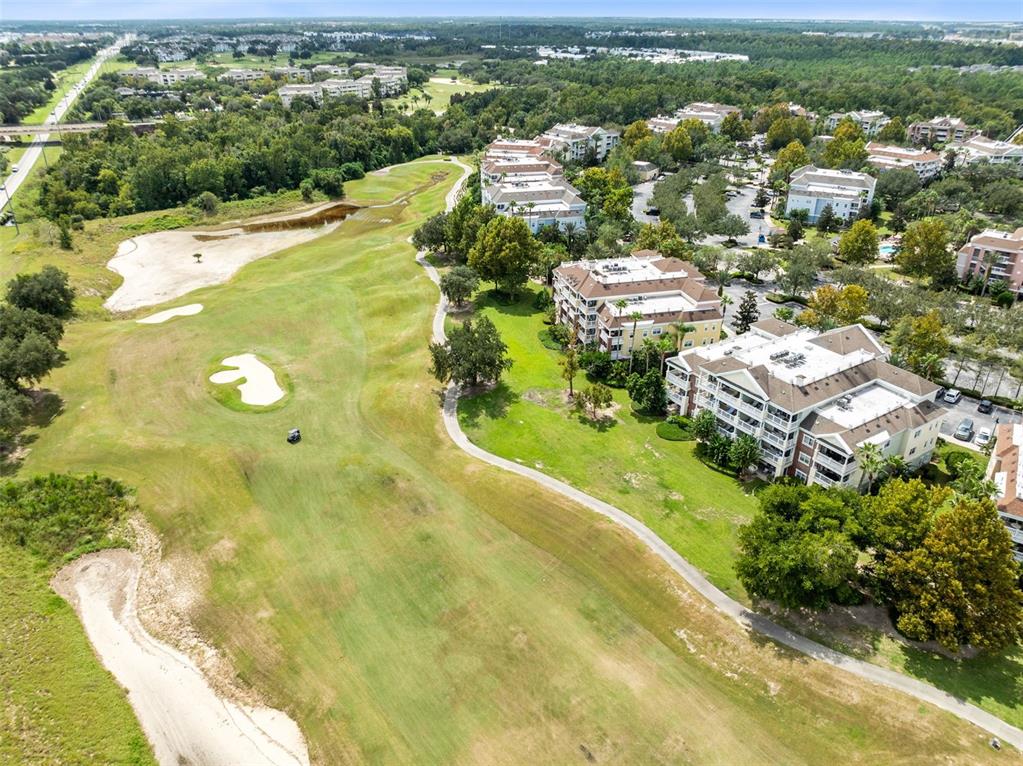 An aerial view shows a golf course fairway adjacent to multi-story residential apartment buildings — 7602 CABANA COURT UNIT 101, KISSIMMEE, FL