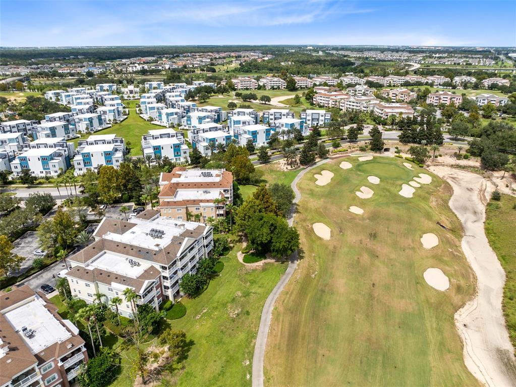 An aerial view shows multi-story apartment buildings adjacent to a golf course with sand bunkers — 7602 CABANA COURT UNIT 101, KISSIMMEE, FL