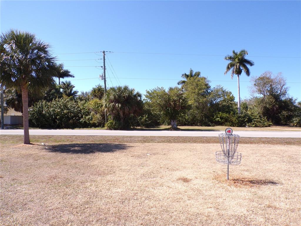 A disc golf basket stands on a grassy field near a road and trees — 711 COOPER STREET, PUNTA GORDA, FL