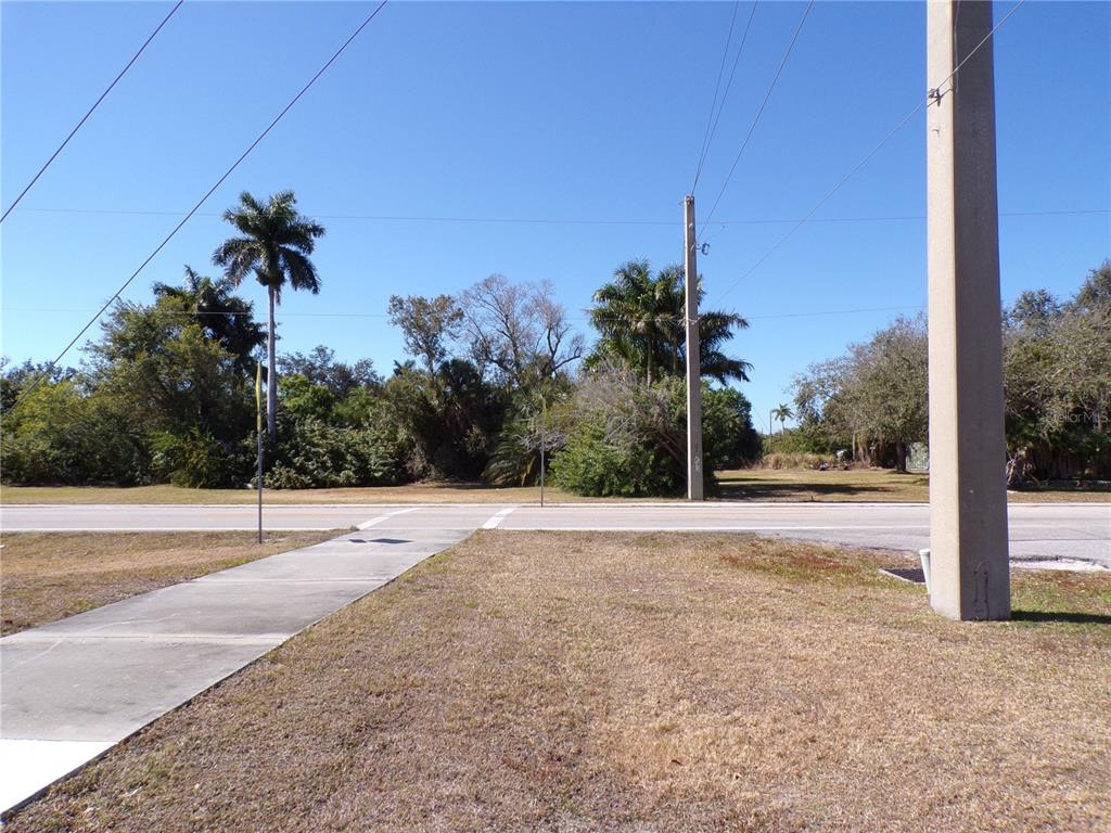 A view of a vacant, grassy lot across a paved road with utility poles — 711 COOPER STREET, PUNTA GORDA, FL